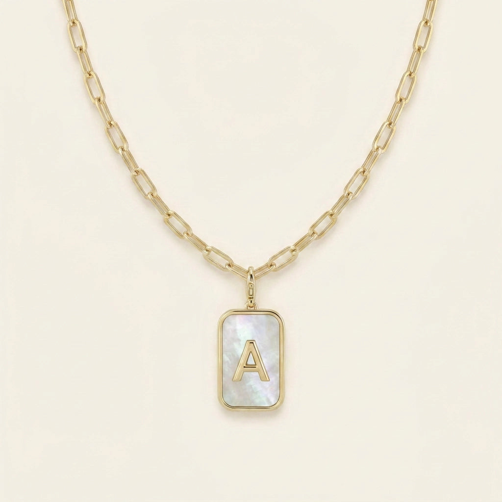Mother of pearl initial card necklace hero — gold-framed pendant mother of pearl with raised gold letter A on paperclip chain, off-white neutral background matching reference