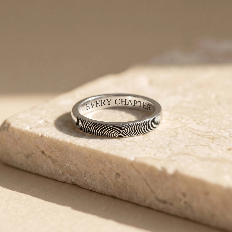 Custom Fingerprint Ring on travertine marble — slim silver, fingerprint wrap, every chapter inside