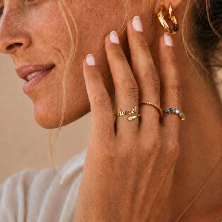 Custom Name Birthstone Ring — gold hazel script worn by a woman, hand against cheek