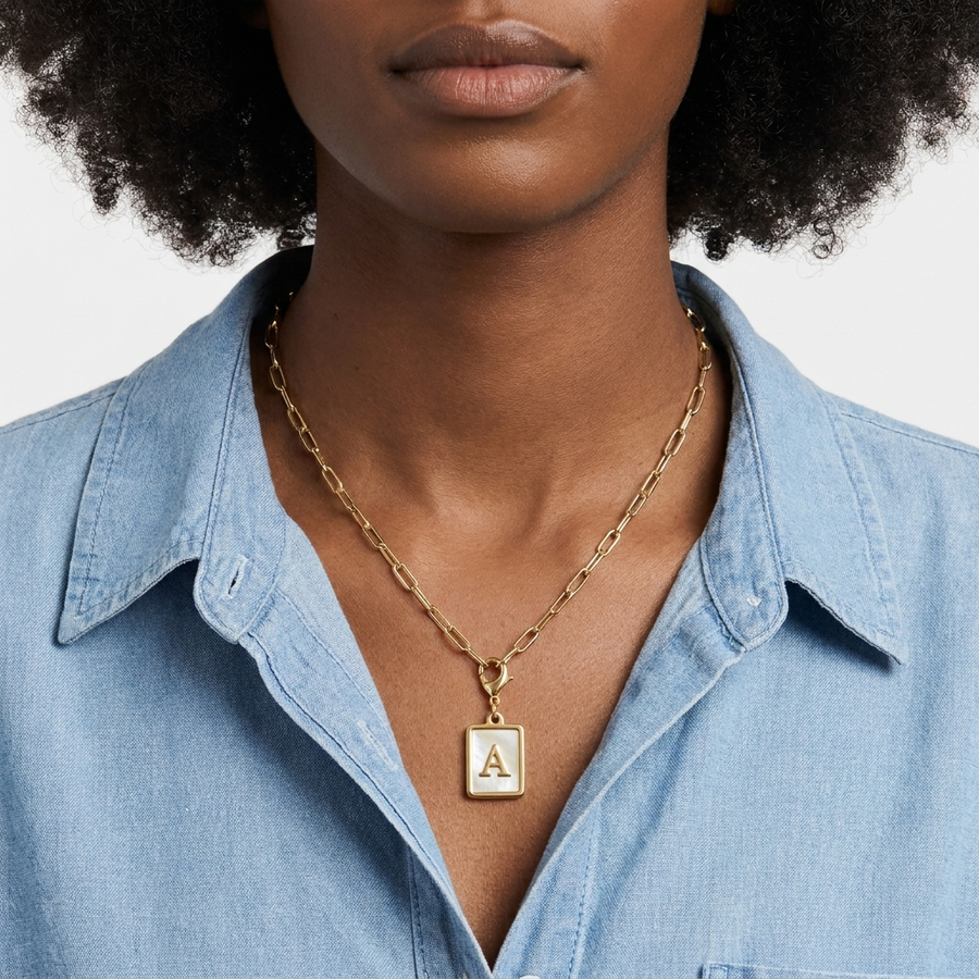 Mother of pearl initial card necklace worn by Black woman with afro hair — iridescent letter A on Gold paperclip chain