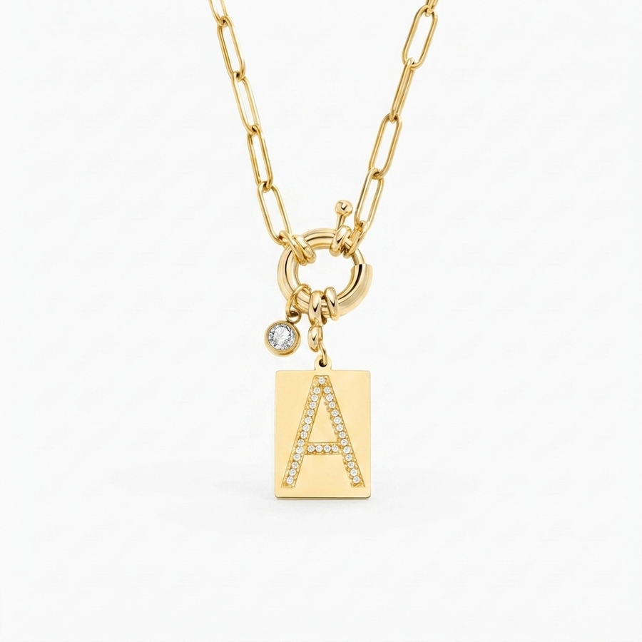 Pave initial pendant necklace hero — gold tag pendant pavé crystal letter A on paperclip chain, off-white neutral background matching reference