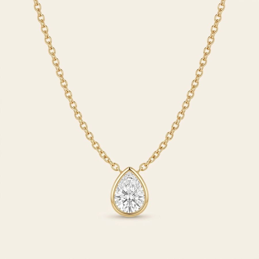 Diamond Teardrop Necklace — single strand cable chain U-curve, cream ivory background, gold bezel pear pendant